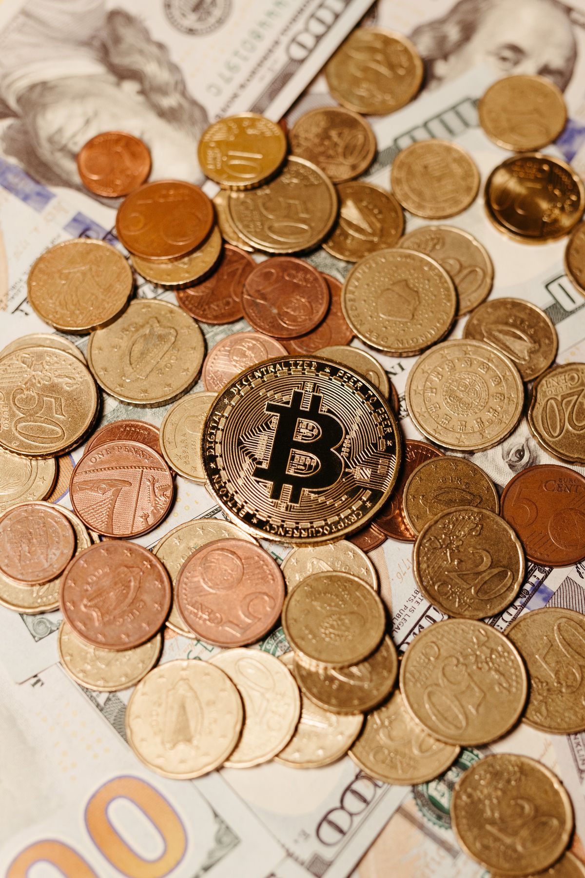 Moneta z symbolem bitcoina wśród monet euro i banknotów dolarowych